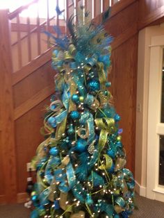 a christmas tree with blue and green decorations on it in front of a stair case