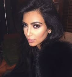 a woman with long black hair is wearing a fur coat and diamond earrings