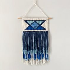 a blue and white wall hanging with tassels on the bottom, in front of a white wall