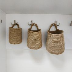 three baskets hanging from hooks on a white wall with two handles in the middle, and one is made out of jute