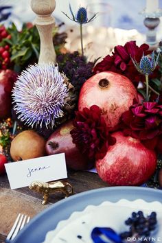 an arrangement of fruits and flowers on a table with a place card in the middle