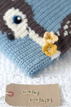 a knitted blue and gray elephant pillow with tag next to it that says new baby