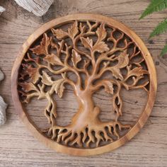 a carved wooden plaque with a tree on it and some leaves around the edges, sitting on a table next to rocks