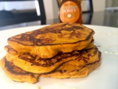 a stack of pancakes sitting on top of a white plate next to a bottle of syrup