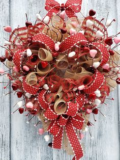 a heart shaped wreath with red and white ribbons on a wooden surface, decorated with hearts