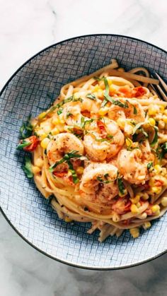 a bowl filled with pasta and shrimp on top of a marble countertop next to a fork