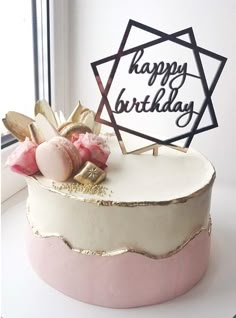 a white and pink birthday cake sitting on top of a table next to a window