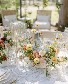 a table topped with lots of vases filled with flowers next to glasses and plates