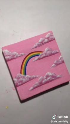 a pink square with clouds and a rainbow painted on the side, sitting on top of a table