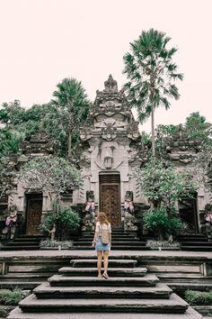 a woman standing on steps in front of a building with trees and bushes around it