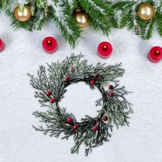 a christmas wreath surrounded by ornaments and balls in the snow with red baubles