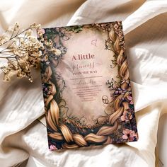 a wedding card with braids and flowers on top of a white bed sheet next to it