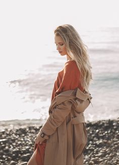 a woman walking on the beach in a trench coat