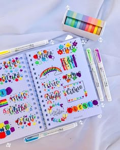 an open notebook with markers, pens and stickers next to it on a bed