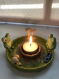 a candle that is sitting on top of a plate with some little frogs around it