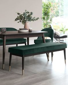 a dining room table with green chairs and a bench in front of it, next to a potted plant