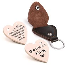 two heart shaped key chains with engraved words on them, one has a leather case and the other has a personalized tag