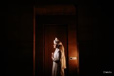 a woman standing in front of a door wearing a white hat and scarf on her head