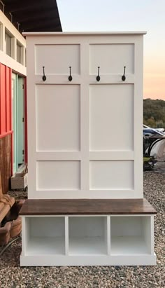 a white wooden bench sitting in front of a red and white building with hooks on it's doors