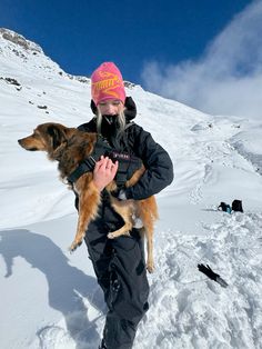 a woman holding two dogs in her arms on top of a snow covered mountain side