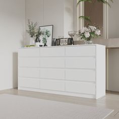 a white dresser sitting in the middle of a living room next to a mirror and potted plant