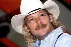 a man with long hair wearing a white cowboy hat and blue striped shirt, looking to the side