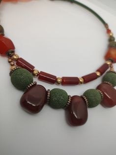 Beautiful handmade double strand choker necklace with various semi-precious stones. The central part is made with large agate beads alternating with large green lava stone beads. Then there is the second strand with long carnelian beads and golden lava beads. The necklace on the back is finished with a green silicone cord. The necklace is very beautiful due to the contrast created between the red of the agate and the carnelian and the green of the lava stone. The necklace is very elegant but at the same time has a touch of retro style, perfect for warm autumn evenings. The necklace is 49cm long, it is made with rigid memory wire, so it holds its shape well and is very comfortable to wear. The closure is a lobster clasp with a 9 cm extension. Perfect for those who love boho and elegant styl Handmade Double Strand Agate Beaded Necklace, Bohemian Jade Necklace With Natural Stones, Bohemian Multi-strand Agate Necklace, Bohemian Jade Necklace With Colorful Beads, Bohemian Carnelian Stone Necklace, Bohemian Double Strand Agate Necklace, Artisan Adjustable Double Strand Necklace, Handmade Double Strand Agate Necklace, Double Strand Agate Beaded Necklaces