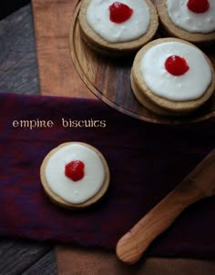 four cookies with white frosting and cherries are on a wooden platter next to a knife