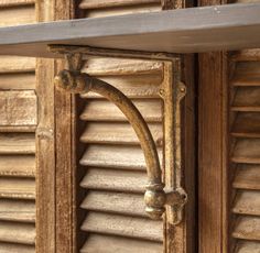 an old wooden shelf with metal brackets on the top and bottom, in front of shutters