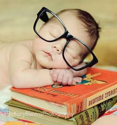 a baby wearing glasses laying on top of books with his head resting on the book