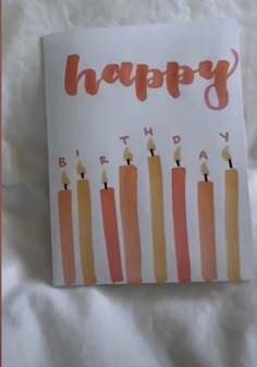 a happy birthday card with candles on it sitting on top of a white bed sheet