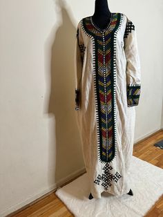 Ethiopian and Eritrean traditional dress (habesh kemis gonder kemis)garment featuring colorful and intricate embroidery. This style is often seen in Ethiopian or Eritrean cultural clothing, known as "Habesha kemis." The dress is typically worn by women for special occasions and celebrations. The garment in   likely  white cotton or linen and adorned with detailed patterns along the neckline, cuffs, and front panel, reflecting the rich textile heritage of the region. White Folk Habesha Kemis For Traditional Ceremonies, Traditional White Kaftan For Festivals, Ceremonial White Traditional Wear With Weaving Work, Bohemian White Traditional Wear With Patterns, Bohemian Style Habesha Kemis For Eid, Bohemian Style Habesha Kemis For Eid With Traditional Drape, Traditional Multicolor Kaftan With Resham Embroidery, Traditional Kurta With Weaving Work For Ceremonies, Bohemian Habesha Kemis For Eid With Traditional Drape