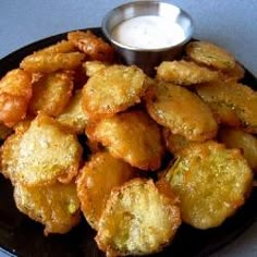 some fried food on a black plate with a small bowl of ranch dressing in the background