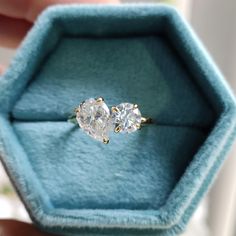 an engagement ring with two pear shaped diamonds sits in a blue velvet box on top of a window sill