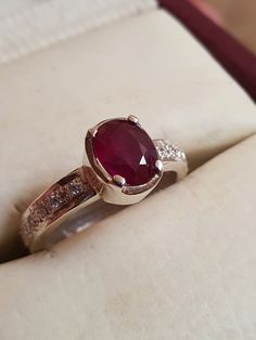 an engagement ring with a large red stone surrounded by small white diamonds on a cushioned surface