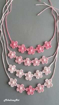 crocheted necklaces with pink and white flowers are displayed on a gray surface