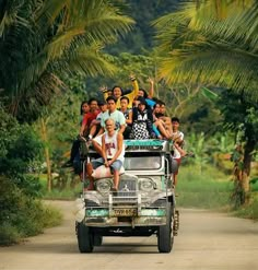 a group of people riding on the back of a truck down a dirt road next to palm trees