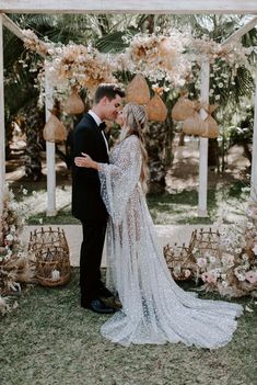 a bride and groom standing in front of an outdoor ceremony arch with flowers on it