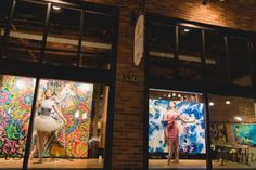 two women are standing in the window of a clothing store with their dresses on display