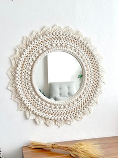 a white crocheted mirror hanging on the wall next to a wooden table and chair