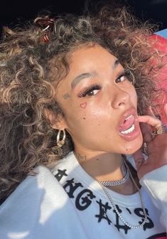 a woman with curly hair and piercings talking on her cell phone while sitting in the back seat of a car