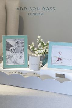 two frames sitting on top of a white table next to flowers and a vase with baby's breath in it