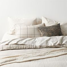 an unmade bed with white linens and plaid pillow cases on top of it