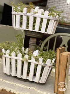 two white baskets filled with plants sitting on top of a table next to an open book