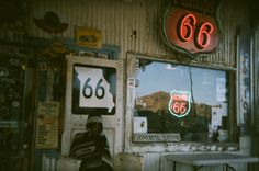 an old gas station with neon signs on the wall and a woman sitting in front of it