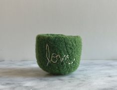 a small green bowl with the word love written on it's side sitting on a marble surface