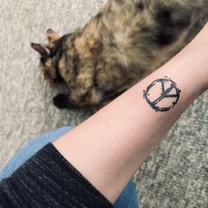 a cat laying on the floor next to a person's arm with a peace sign tattoo