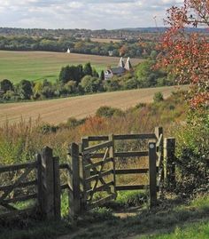 a wooden gate in the middle of a field with trees and fields behind it,