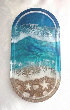 a glass plate with sand and starfish on the beach next to the ocean waves