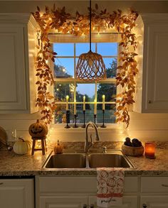 a kitchen sink under a window covered in fall leaves and pumpkins next to candles